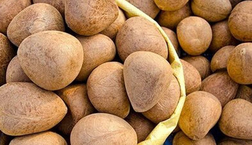 A close-up pile of brown oval-shaped coconuts with a yellow woven carrier partially visible behind them.