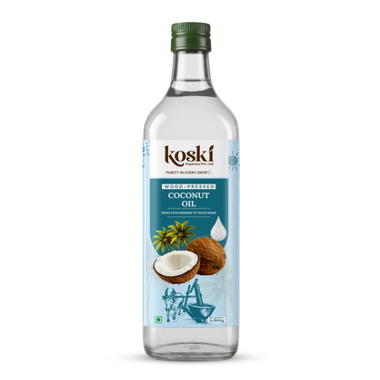 A bottle of Koski WoodPressed Coconut Oil on a clean white background. The clear glass bottle features a green screw cap and a light blue label with illustrations of a coconut, green leaves, and a traditional coconut oil grinder