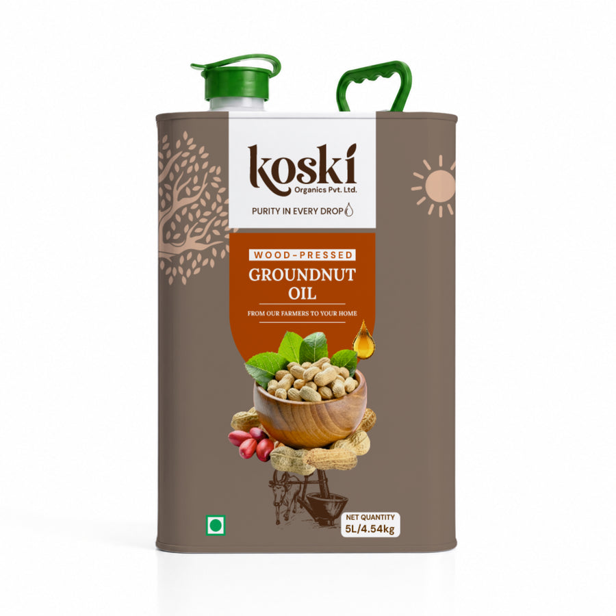 A 5L metal can of Koski Organic Groundnut Oil with a brown body, green plastic cap and handle, and a central label showing peanuts, ginger, and green leaves