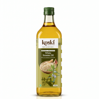 A 900ml bottle of Koski White Sesame Oil on a clean white background. The clear glass bottle shows the golden-yellow oil inside, topped with a dark green cap and featuring a white and green label with illustrations of sesame seeds and herbs