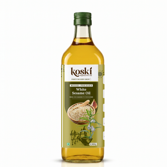 A 900ml bottle of Koski White Sesame Oil on a clean white background. The clear glass bottle shows the golden-yellow oil inside, topped with a dark green cap and featuring a white and green label with illustrations of sesame seeds and herbs